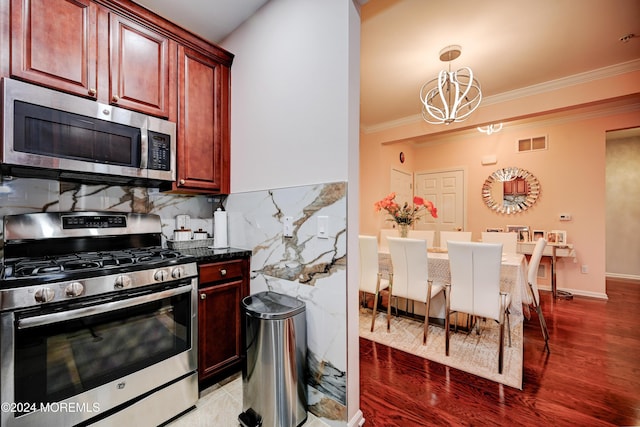 kitchen with appliances with stainless steel finishes, wood-type flooring, a chandelier, decorative backsplash, and crown molding