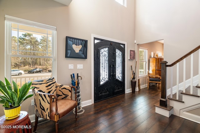 foyer entrance with baseboards, a towering ceiling, wood-type flooring, stairs, and french doors