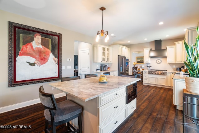 kitchen featuring light stone countertops, wall chimney range hood, stainless steel gas stovetop, and dark wood-style floors