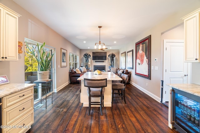 dining room featuring dark wood-style floors, wine cooler, baseboards, and a fireplace