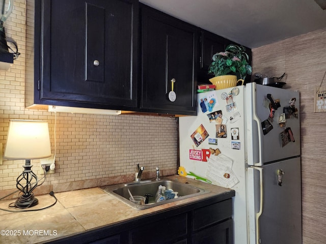 kitchen featuring light countertops, a sink, freestanding refrigerator, and dark cabinets