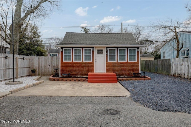 bungalow-style home with a patio area, a fenced backyard, and roof with shingles