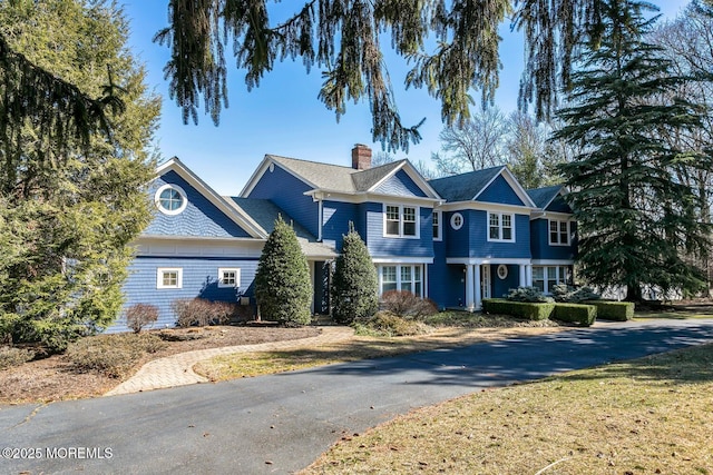 shingle-style home with driveway and a chimney