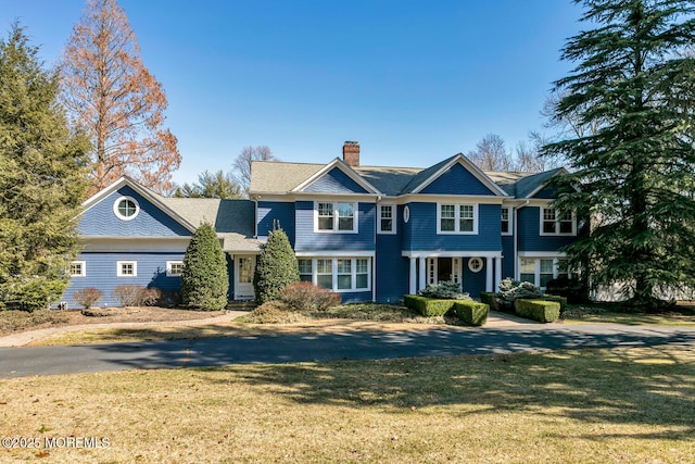 shingle-style home featuring a front yard and a chimney