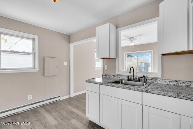 kitchen featuring sink, baseboard heating, white cabinetry, light hardwood / wood-style floors, and stone countertops