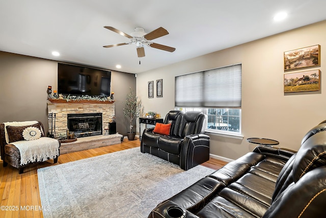 living room with ceiling fan, wood-type flooring, and a stone fireplace