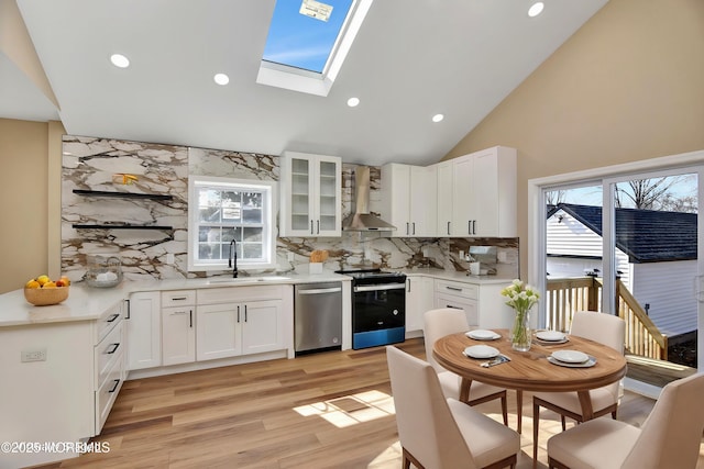 kitchen with electric stove, wall chimney exhaust hood, white cabinets, stainless steel dishwasher, and sink