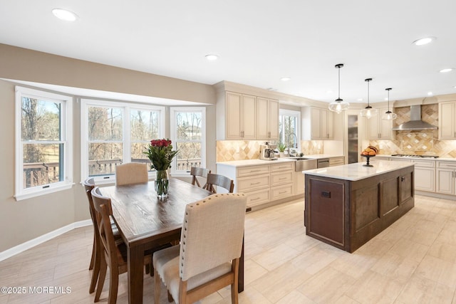 kitchen with wall chimney range hood, a center island, cream cabinetry, and decorative light fixtures