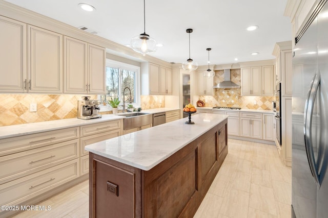 kitchen featuring cream cabinetry, sink, appliances with stainless steel finishes, wall chimney exhaust hood, and pendant lighting