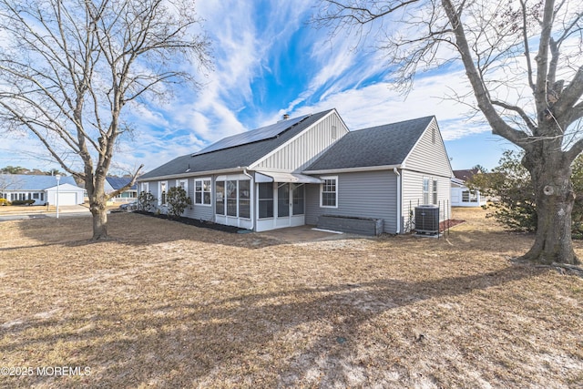 back of property featuring a sunroom, roof with shingles, central air condition unit, a patio area, and roof mounted solar panels