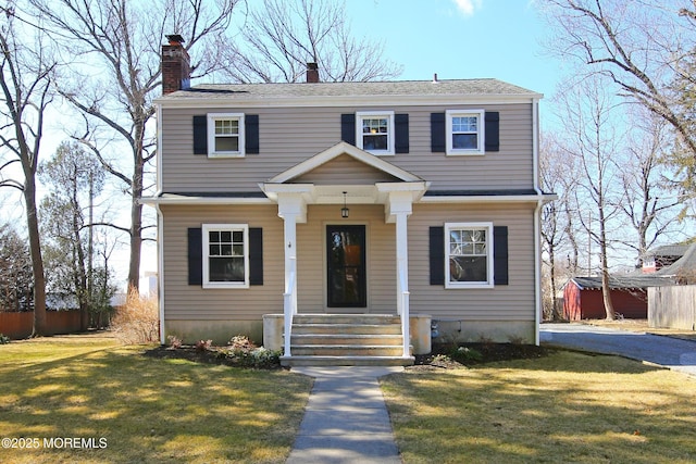 view of front of house with covered porch, fence, a chimney, and a front lawn