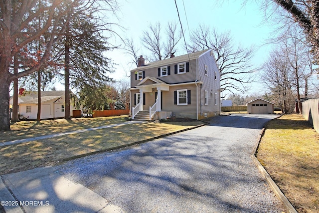 colonial house with an outbuilding, a chimney, fence, a garage, and driveway