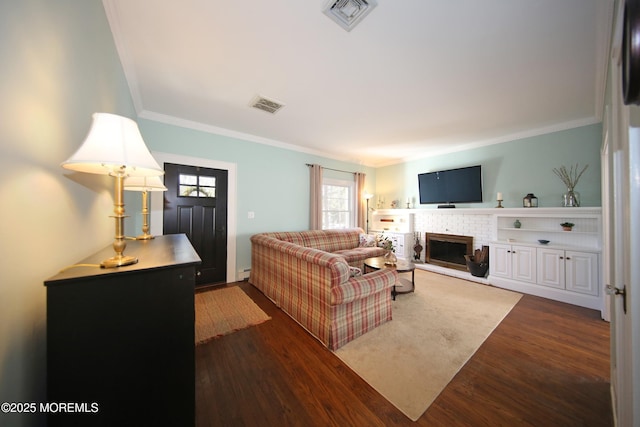 living room with ornamental molding, a brick fireplace, wood finished floors, and visible vents