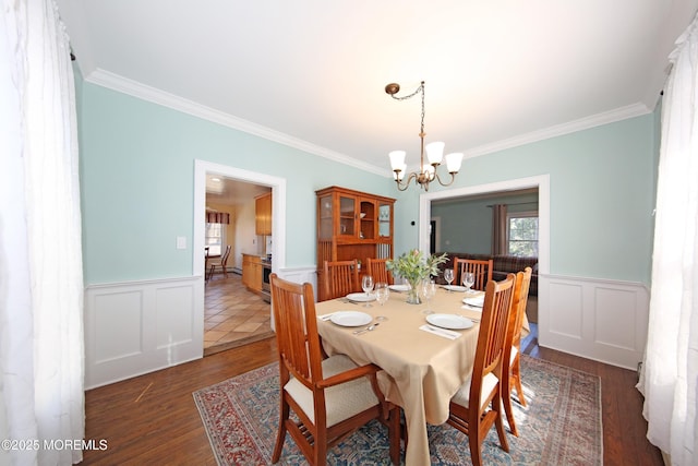 dining area featuring a chandelier, ornamental molding, wood finished floors, and wainscoting