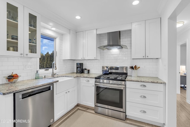 kitchen with appliances with stainless steel finishes, white cabinets, light stone counters, and wall chimney range hood