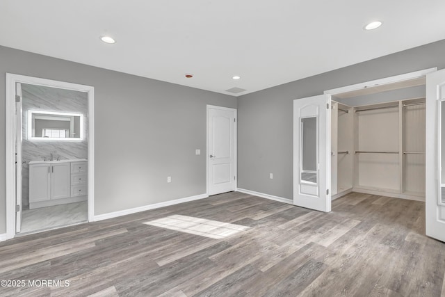 unfurnished bedroom featuring a walk in closet, ensuite bath, light hardwood / wood-style floors, and a closet