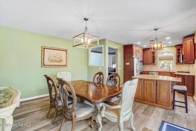 dining space with an inviting chandelier, sink, and light hardwood / wood-style flooring