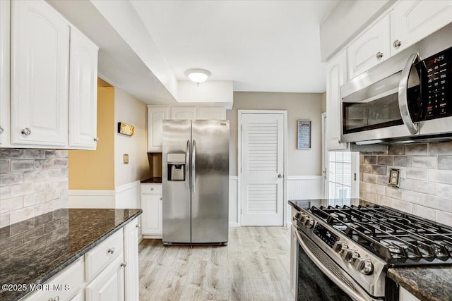 kitchen with appliances with stainless steel finishes, dark stone counters, light hardwood / wood-style floors, white cabinets, and decorative backsplash