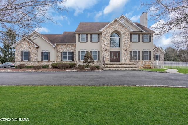 view of front of home featuring aphalt driveway, a chimney, a front yard, and stucco siding