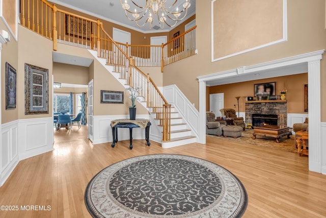 foyer with stairs, a stone fireplace, wood finished floors, and an inviting chandelier