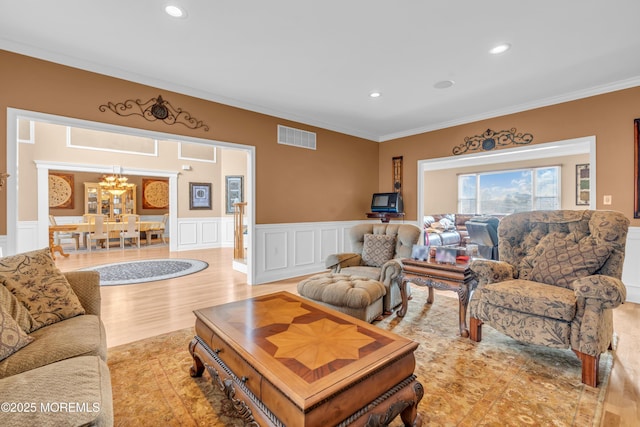 living area featuring wainscoting, recessed lighting, visible vents, and ornamental molding