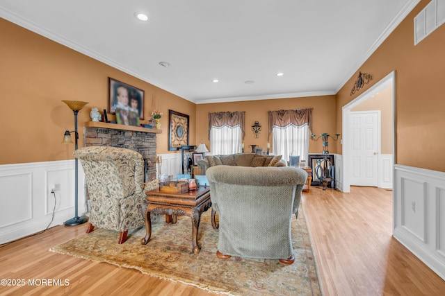 living room with light wood-style floors, a fireplace, visible vents, and crown molding