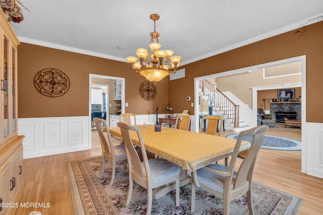 dining room featuring ornamental molding, a stone fireplace, and light wood-style flooring