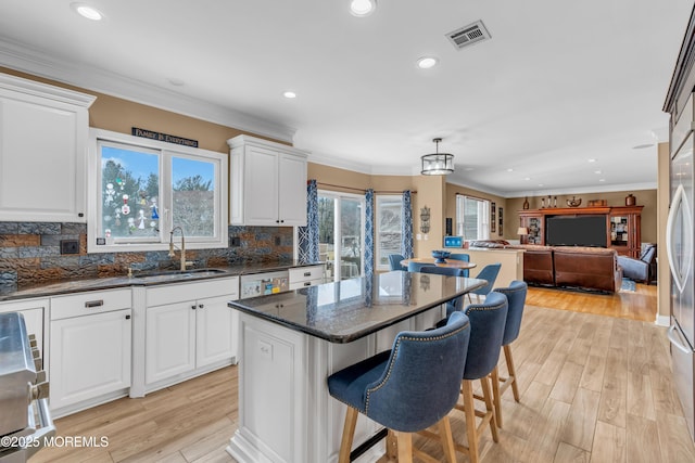 kitchen featuring hanging light fixtures, open floor plan, white cabinets, a kitchen island, and a sink