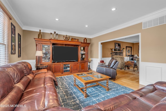 living area with ornamental molding, a wainscoted wall, visible vents, and light wood-style flooring