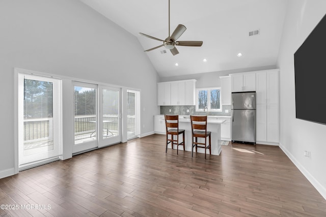 kitchen with visible vents, white cabinets, a kitchen island, a breakfast bar, and freestanding refrigerator