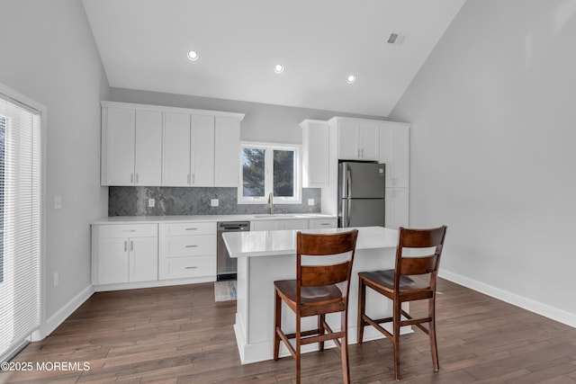 kitchen with tasteful backsplash, white cabinets, appliances with stainless steel finishes, light countertops, and a kitchen bar