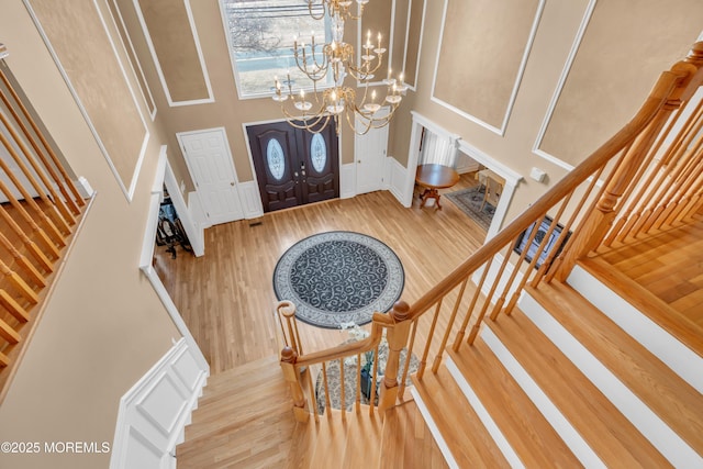 foyer featuring a decorative wall, stairway, a high ceiling, an inviting chandelier, and wood finished floors