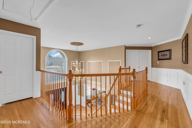 hall with attic access, an upstairs landing, light wood-style floors, a chandelier, and a decorative wall