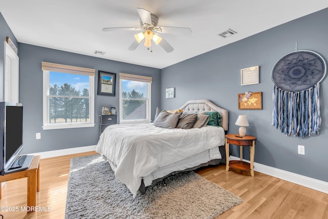 bedroom with a ceiling fan, visible vents, baseboards, and wood finished floors