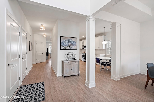 corridor with light hardwood / wood-style floors and decorative columns