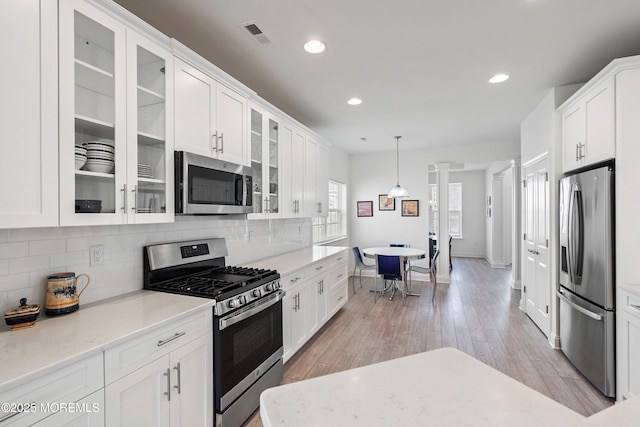 kitchen featuring hanging light fixtures, ornate columns, white cabinetry, and stainless steel appliances