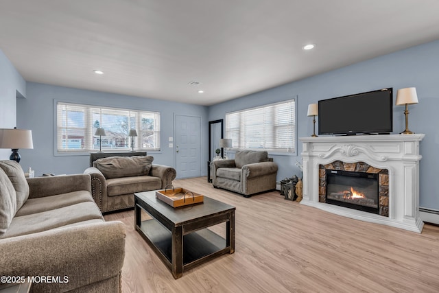 living area featuring light wood-type flooring, a glass covered fireplace, visible vents, and recessed lighting