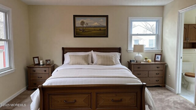 carpeted bedroom with ensuite bath and baseboards