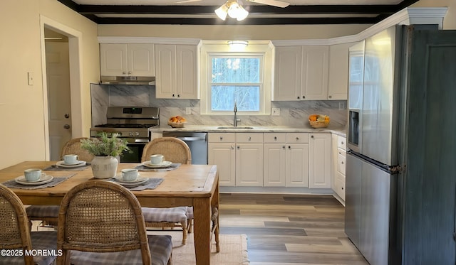 kitchen with a sink, stainless steel appliances, under cabinet range hood, white cabinetry, and light wood-type flooring