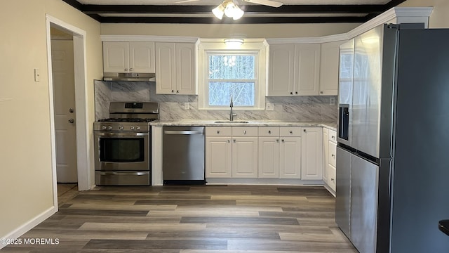 kitchen with under cabinet range hood, appliances with stainless steel finishes, white cabinets, and a sink