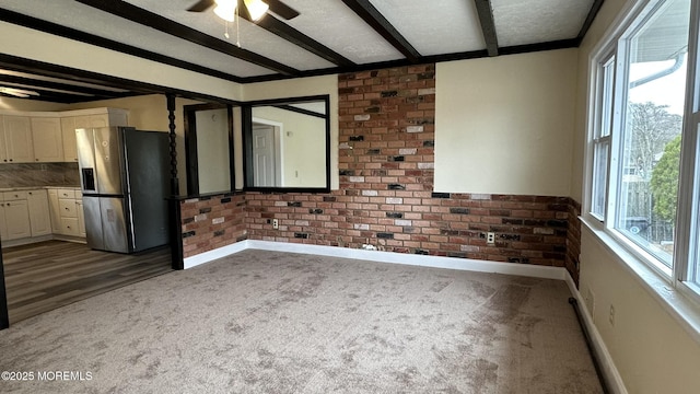 carpeted spare room featuring beamed ceiling, brick wall, and a wealth of natural light