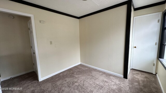 unfurnished bedroom featuring a textured ceiling, baseboards, crown molding, and carpet