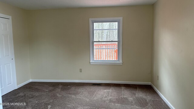 spare room featuring baseboards and dark carpet