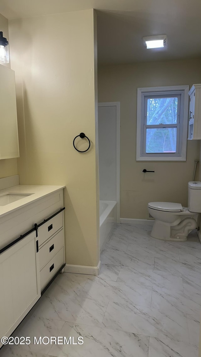 bathroom featuring baseboards, a washtub, toilet, marble finish floor, and vanity