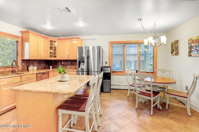 kitchen featuring appliances with stainless steel finishes, light brown cabinetry, decorative light fixtures, a kitchen island, and sink