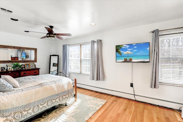 bedroom featuring hardwood / wood-style flooring, ceiling fan, and a baseboard heating unit