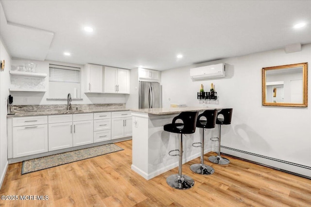 kitchen featuring an AC wall unit, stainless steel refrigerator, sink, light stone counters, and white cabinets