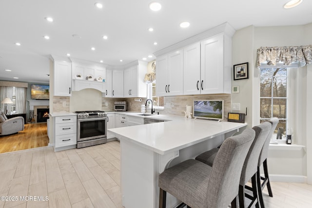 kitchen featuring light countertops, white cabinetry, stainless steel gas range, a lit fireplace, and a kitchen breakfast bar