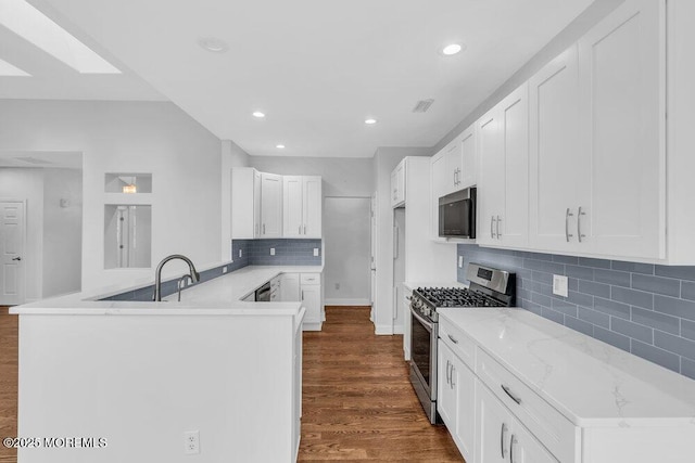 kitchen featuring kitchen peninsula, sink, stainless steel gas range oven, white cabinets, and dark hardwood / wood-style floors