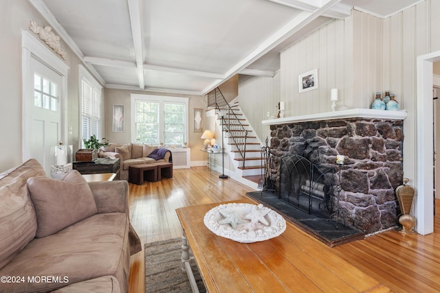 living room with beam ceiling, hardwood / wood-style flooring, a stone fireplace, baseboards, and stairs